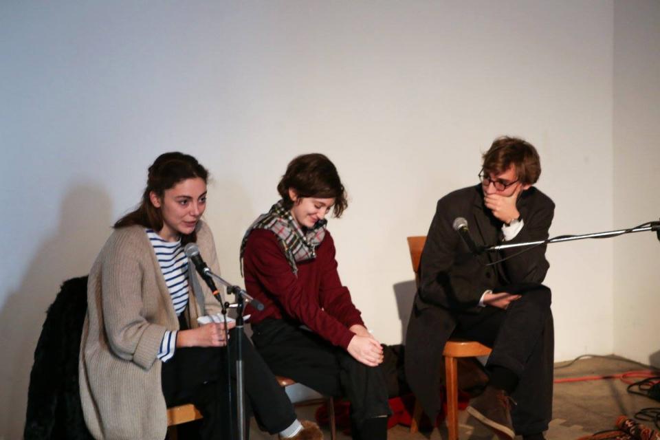 Three people sitting in front of microphones, holding a reading
